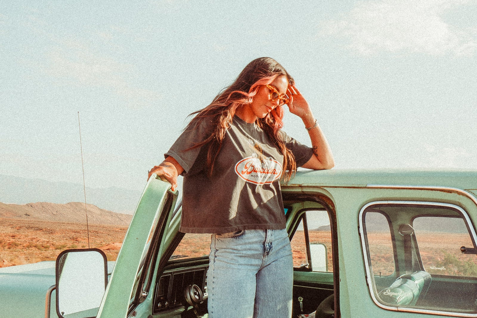 Person standing next to a vintage green car with a scenic background
