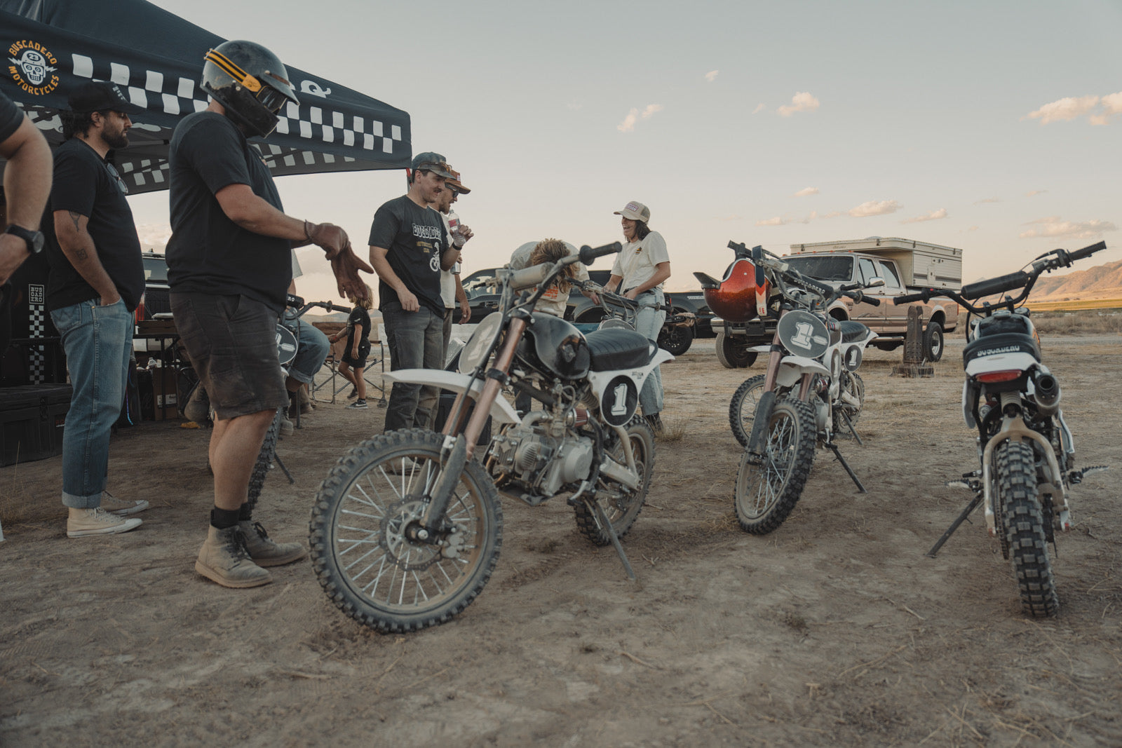 Friends laughing and talking beside BSX 110 and BSX 140 bikes at camp after a ride